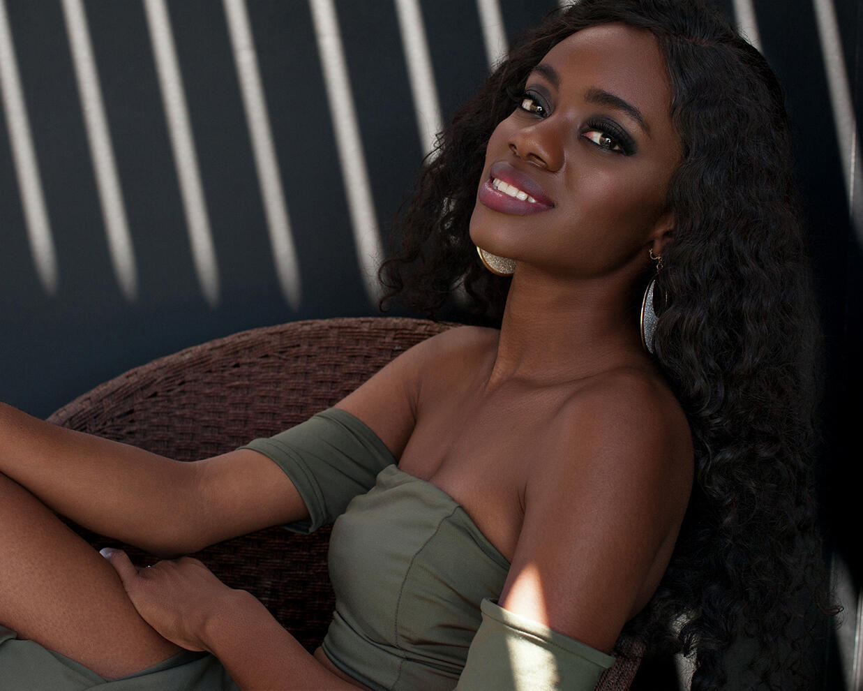 Black female model smiling reclining in a chair with shafts of sunlight behind by Tampa photographer Sidney Oster