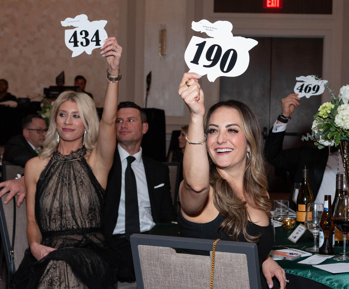 Two women holding up bid signs at a corporate charity auction event