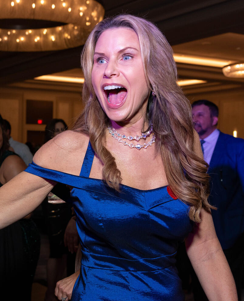 Woman wearing a blue gown screaming in happy excitement at a corporate event party