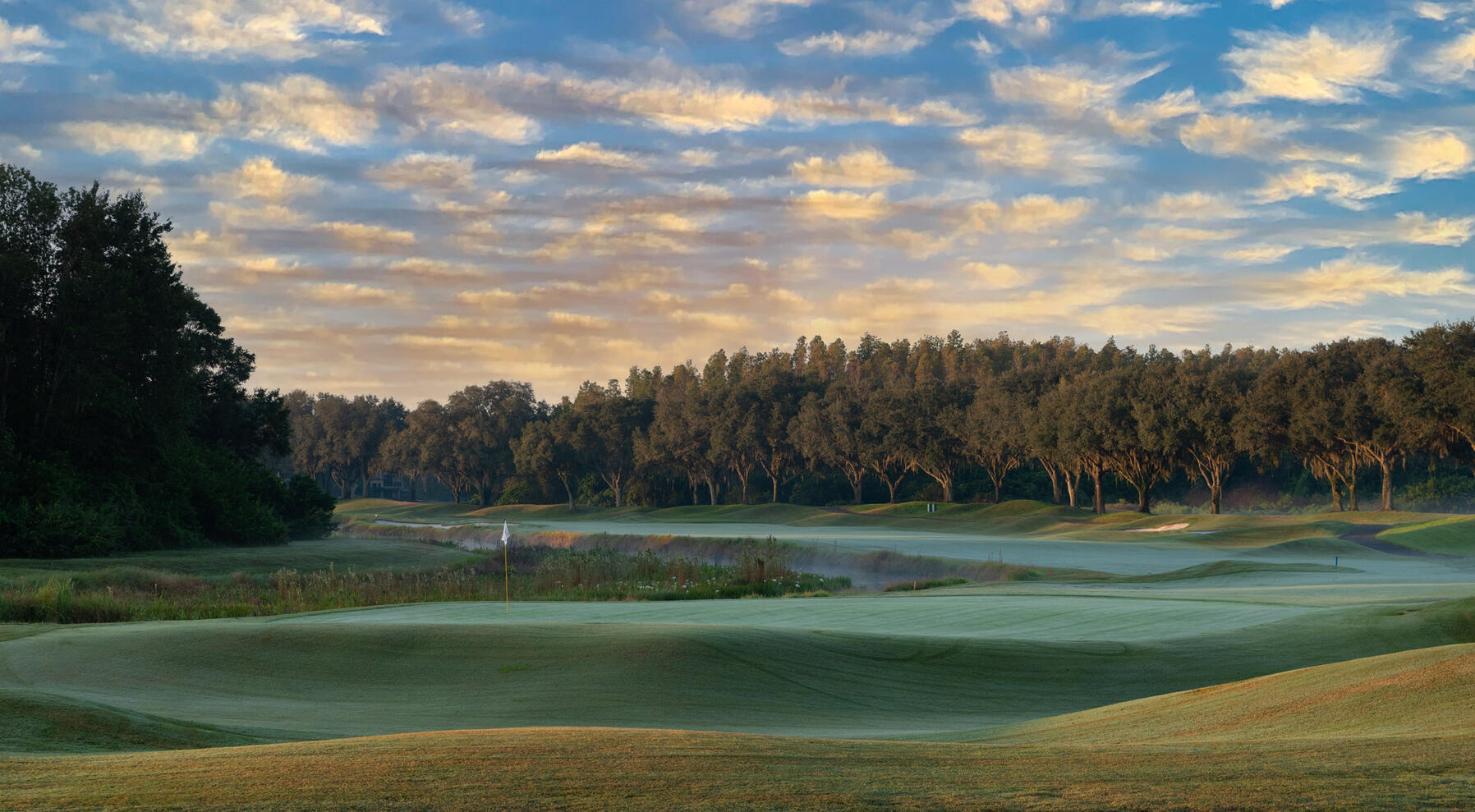 Golf course 18th hole with a light mist and clouds in the sky during sunset